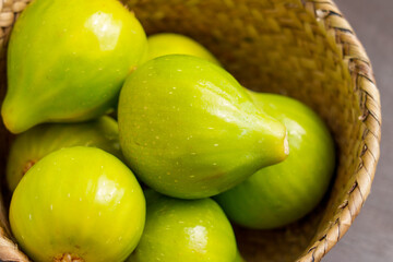 Green freshly picked juicy figs in a wicker eco-friendly bowl close up. Fruits harvest concept