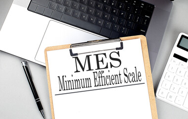 MES minimum efficient scale written on clipboard with laptop and calculator
