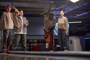 Group of friends enjoying bowling game together in recreational complex, mingling and sharing laughs while showing different emotions from joy to concentration