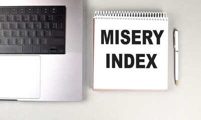Misery index concept on notebook with laptop and pen on gray desk