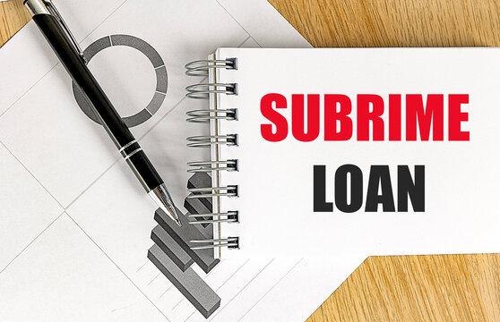 Subprime loan concept in a spiral notebook with pen and charts on a wooden desk