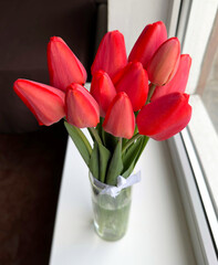 Fresh red tulips in a glass vase on the windowsill