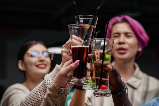 Three friends enjoying drinks at gathering while raising glasses in toast. Smiling and showing camaraderie, each holding different beverage in lively social setting