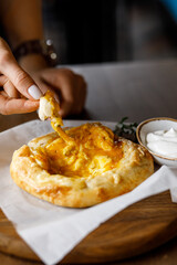 handsome girll is eating delicious khachapuri with juicy meat, fresh vegetables, fragrant herbs, and crispy dough on a beautiful white plate in a cozy nice restaurant