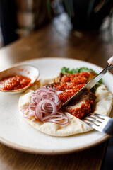 handsome man is eating delicious dish with juicy chicken, fresh vegetables, and crispy lavash, served with adjika sauce and fragrant herbs on a beautiful white plate on a wooden table 