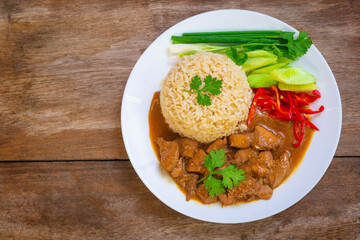 Chinese style chicken gravy fragrant with sesame oil and steamed jasmine brown rice with side dishes of scallions, cucumber, cilantro, red chilli in white plate on wooden table.