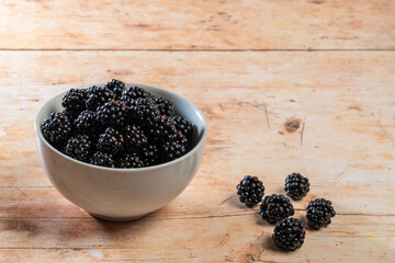 Cultivated fresh large juicy blackberries in white bowl on wooden top.