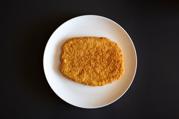 Raw, golden, bread crumb chicken schnitzel on a white plate. Top view, no people