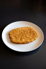 Raw, golden, bread crumb chicken schnitzel on a white plate. Top view, no people