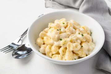 Macaroni cheese in bowl with spoon and fork on white background