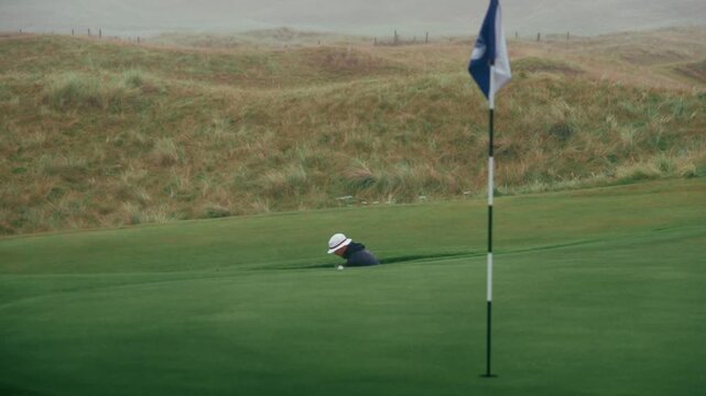 Golfer hits bunker shot and lips out almost holing out in slow motion on Irish links course on foggy rainy day