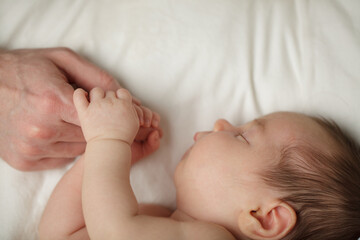 Adorable Newborn Baby Sleeping with father hand on White Bed Background with copy space