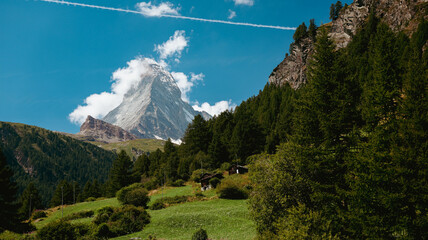 Matterhorn Mountain towers over lush green fields and pine forests in Zermatt, Switzerland,...