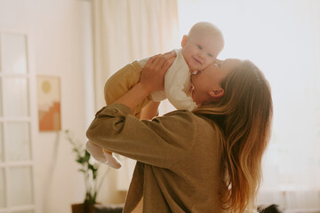Mother holding her baby in cozy living room setting with warm natural light, creating intimate and...