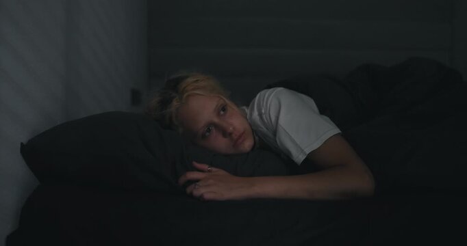 A young blonde girl in a white T-shirt wakes up abruptly while lying in a serious bed
