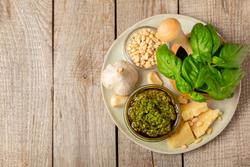Pesto. Italian basil pesto sauce on a textured wooden background. Ingredient for pesto sauce: fresh basil, pine nuts, Parmesan cheese and olive oil. Space for text.Copy space.