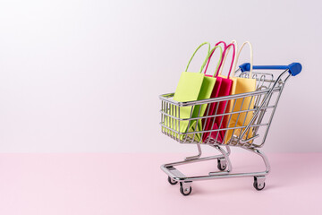 Colorful paper shopping bags in shopping trolley on bright background. Creative minimal shopping concept.