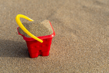 Red sand castle bucket on a sand background. Minimal summer vacation concept.