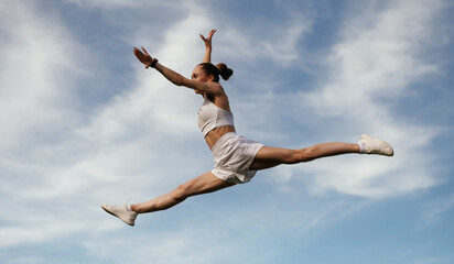 Blue sky with clouds, jumping. Young skinny fitness woman is outdoors