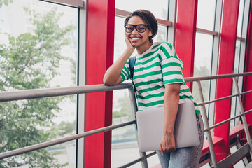 Portrait of nice young woman hold laptop striped t-shirt backpack work study business center office