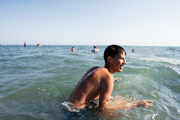 Teenage boy enjoying a sunny day swimming in the ocean with others in the background