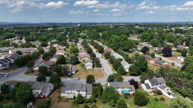 American Suburban neighborhood with neatly arranged home buildings in Pennsylvania. Residential streets and green lawns. Row of houses with grey roof. Aerial truck wide shot in summer.