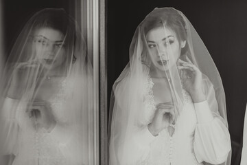 A woman in a wedding dress is standing in front of a mirror with a veil covering her face