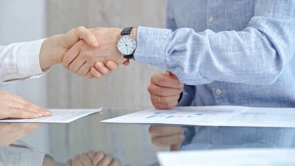 Business people shaking hands over contract agreement and financial papers at the glass table. Professional handshake, close up