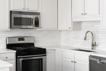 A kitchen detail with white cabinets, a brushed gold faucet, marble countertop, and a marble subway tile backsplash.