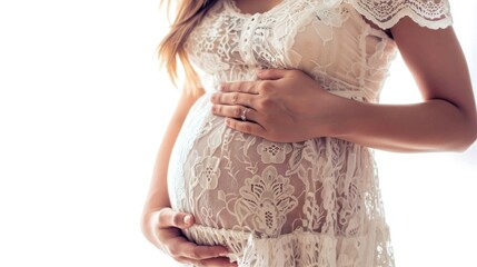 Pregnant woman in a white lace dress gently cradling her baby bump in soft natural light