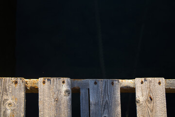 edge of a wooden pier or bridge where we also see the waters of the sea in the background with rocks and sunken ropes