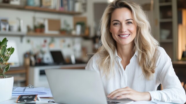 A blonde woman with a cheerful demeanor is working on her laptop in a stylish home office setting, showcasing the joys and productivity of a balanced remote work lifestyle.