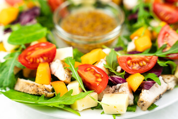 Healthy salad from chicken, tomatoes, cheese and arugula leaves with honey mustard sauce. Close-up. Selective focus.