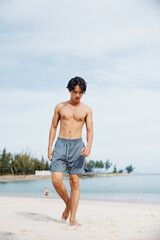 Active Lifestyle: Muscular Asian Man Running on Beach at Sunset, Exuding Strength and Freedom