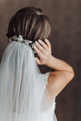 A woman with a white veil and a gold flower headpiece. She is holding her hand up to her ear