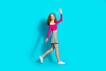 Full body portrait of lovely young girl walk arm wave hi wear top isolated on turquoise color...