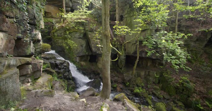 Wide tilting down shot of the Lumsdale waterfalls with rocks and trees in foreground at Lumsdale, Matlock