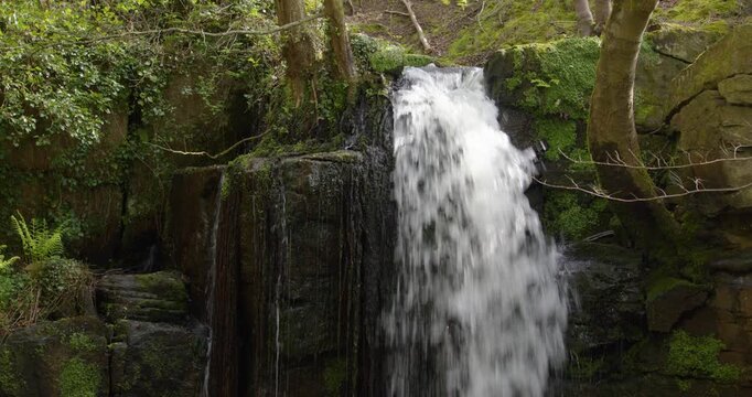 Mid shot looking straight on right of frame of the Lumsdale waterfalls with rocks and trees at Lumsdale, Matlock