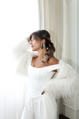 In a light-filled room, a beautiful brunette of middle age is seen wearing a white outfit