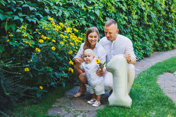 Loving parents mom and dad celebrate one year of their son in nature. Happy family hugging their little son.