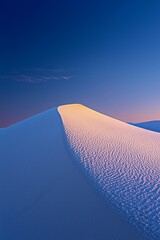 A bright white sand dune contrasted against a deep blue sky at sunset.