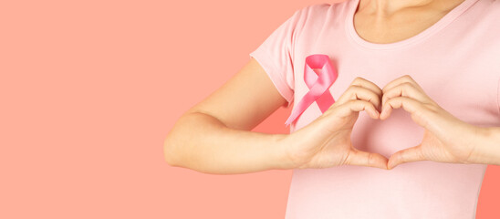 Breast Cancer Awareness in October. Woman hand made heart shape on her chest with pink ribbon awareness for support people who live with breast cancer. Women's health care concept.