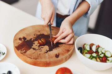 Fresh and colorful salad preparation with tomatoes being sliced on a cutting board, with salad bowls on the table