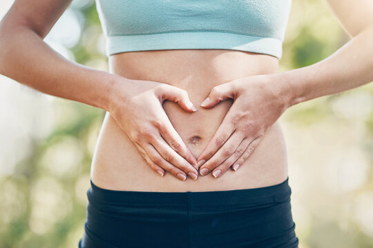 Heart, woman and hands on stomach for fitness, body and wellness outdoor. Abdomen, love and sign for care, digestion or gut health with intermittent fasting to lose weight with hcg diet detox at park