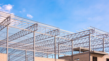 Obraz premium Factory building structure with gray metal columns and roof beam in construction site against blue sky background, low angle and perspective side view
