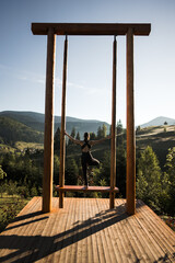 A young woman does yoga on a swing against the background of the mountains. Yoga and meditation concept