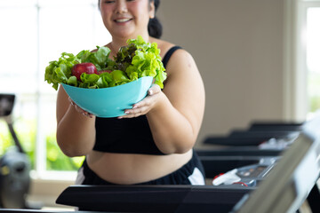 Portrait fat woman enjoying eating vegetable salad. beautiful young chubby overweight woman wearing sporty fitness clothes doing exercise indoors at gym fitness sport club, body and health care