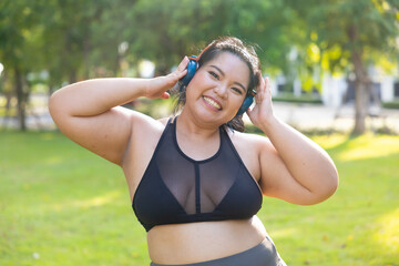 Portrait sportswoman listening music through headphones. beautiful young chubby overweight woman in sportswear doing exercise outdoors at park. fitness sport club, body and health care. Asian female