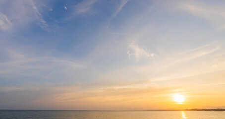Sunset sky clouds over sea in the evening with orange, yellow sunlight on golden hour, horizon sea sky landscape nature background