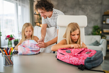 Single father help to his daughters to pack books in a backpack